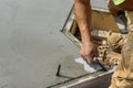 A masonry worker holds a steel trowel and is smoothing a cement floor with plastering concrete