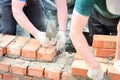 Masons in protection gloves are laying bricks applying mortar, concrete using a trowel to build a brick wall of a house