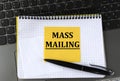 MASS MAILING - words on a yellow piece of paper on the background of a laptop with a notebook and a pen