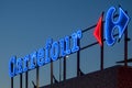 The illuminated neon sign of the French supermarket chain Carrefour at sunset