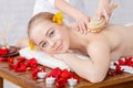 Massage with brush. Smiling girl receives massage on massage table with rose petals Royalty Free Stock Photo