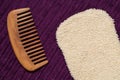 Massage glove and wooden hair comb on purple bath towel