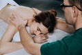 Massage therapist doing shoulder massager of a young woman. Beautiful relaxed face of a young woman with brown hair