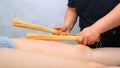 Massage therapist makes an anti-cellulite legs massage to a fat woman on a massage table in a spa with a bamboo stick