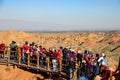 Masses of tourists move along walkway with a stunning view of Rainbow Mountains