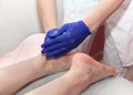 Masseur hands in blue protective gloves touch feet of woman patient doing foot massage procedure in spa salon. Royalty Free Stock Photo