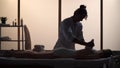 Masseur, massage specialist giving a massage to his patient using herbal bags. Silhouettes of a woman and a man in the