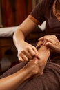 Masseuse stimulating pressure point on patient foot with wooden tool