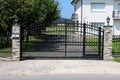 Massive black wrought iron entrance doors with decorations held in place by two stone poles with baroque style street lamps on top Royalty Free Stock Photo