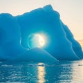 Massive blue iceberg with a smooth, rounded hole at its center. The sun shines Royalty Free Stock Photo