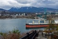 A massive cargo ship navigates under Lions Gate Bridge in Burrard Inlet, with the West Vancouver skyline in the background