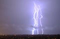 Massive cloud to ground lightning bolts hitting the horizon of city lights