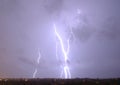 Massive cloud to ground lightning bolts hitting the horizon of city lights