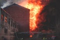 Massive large blaze fire in the city, brick factory building on fire, hell major fire explosion flame blast, with firefighters