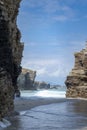 Massive layered rock cliffs frame an ocean view at As Catedrais Beach, Spain. Waves roll onto the wet sand, capturing a Royalty Free Stock Photo