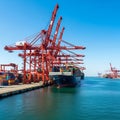 Massive red cranes load cargo ship at busy port under blue sky Royalty Free Stock Photo
