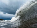 A massive wave crashes in the water on a cloudy day, stirred up by the wind