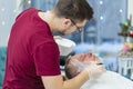 A master applies shaving cream to the beard of an adult man in a hairdressing salon with a shaving brush.