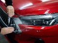 The master applies vinyl film to the headlight of a red car.