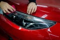 The master applies vinyl film to the headlight of a red car. Closeup view on worker detailer hand smoothing with a