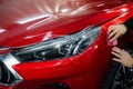 The master applies vinyl film to the headlight of a red car. Closeup view on worker detailer hand smoothing with a