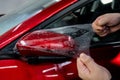 The master applies vinyl film to the side view mirror of a car.