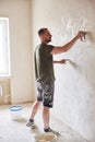 Master is applying white putty on wall and smearing by special knife in room of renovating apartment at daytime Royalty Free Stock Photo