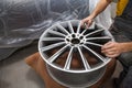 Master body repair man is working on preparing the surface of the aluminum wheel of the car for subsequent painting in the