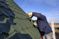 The worker screws the snow retaining elements to the roof with a screwdriver