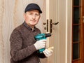 The master with a cordless screwdriver in his hands in the room near the door intends to repair the door lock