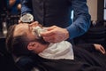 Master hairdresser prepares the face for shaving and smears the face with foam in a hairdressing salon.