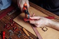 Master holding a hole punch and a piece of leather. On brown wooden table scattered with tools and accessories Royalty Free Stock Photo