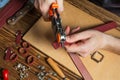 Master holding a hole punch and a piece of leather. On brown wooden table scattered with tools and accessories. Royalty Free Stock Photo