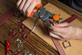 Master holding a hole punch and a piece of leather. On brown wooden table scattered with tools and accessories. Royalty Free Stock Photo