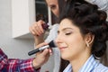 Master inflicts brush powder on the face of the girl, completes the day make-up in a beauty salon. Royalty Free Stock Photo