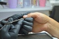 Master of manicure in black gloves makes a cut manicure, trimming the cuticle on finger with scissors Royalty Free Stock Photo