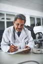 The master of medical science. a mature scientist using a microscope and recording his findings in a laboratory.