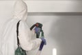 Master painter in white suit paints wall with a spray gun