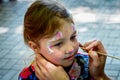 The master paints a beautiful figure on the face of a little girl with a brush. The child is impregnated with makeup in the form Royalty Free Stock Photo