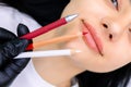 Master of permanent makeup in a black glove holds marking pencils in front of the model`s lips Royalty Free Stock Photo