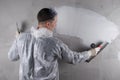 A master in a protective suit is working on leveling the concrete wall with a large spatula, applying a white solution, there is a