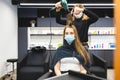 Master woman hairdresser in a medical mask dries the girl's hair with a hairdryer and combs after washing in a beauty Royalty Free Stock Photo