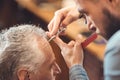 Masterful barber making hairdo of the retired client in barbershop