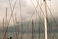 Masts and many ropes of sailing boats standing in harbor. Graphic image with oblique and vertical lines. Cloudy sky in background