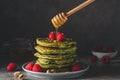 Matcha green pancakes with fresh raspberries, pistachios and flowing honey on dark background. low key Royalty Free Stock Photo