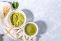 Matcha green tea cup and powder bowl, wooden spoon, bamboo whisk, fresh leaves on napkin on grey textured backdrop. Royalty Free Stock Photo