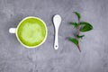 Matcha green tea latte beverage in white ceramic cup with spoon, green leaf