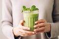 Matcha green vegan smoothie with chia seeds and mint in glass in hands of female