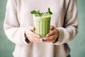 Matcha green vegan smoothie with chia seeds and mint in glass in hands of female