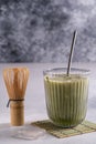 Matcha latte with cream foam in glasses, bamboo whisk tusaku and matcha powder on table